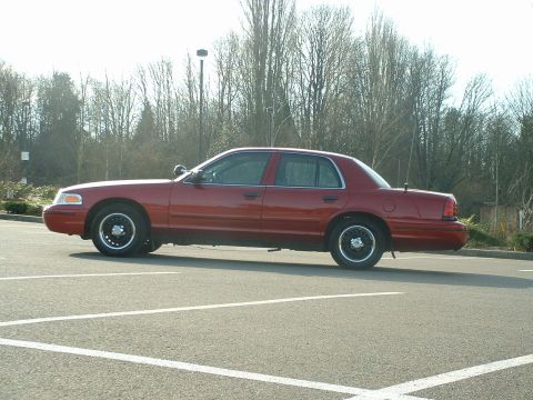 1999 Ford Crown Victoria - A red 1999 Ford Crown Victoria is parked in a lot, seen from the side.
