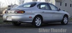 1999 Ford Taurus - A silver sedan is parked on a street with houses in the background.