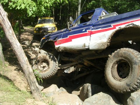 1977 Ford F-150 - A lifted 1977 Ford F-150 navigates a rocky off-road course, with a yellow Jeep in the background.