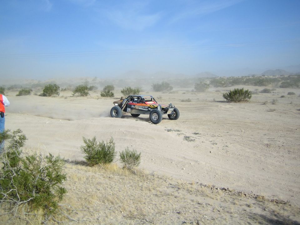 Off-road sand rail buggy racing across desert kicking up dust