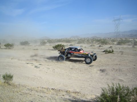 Open-frame desert race buggy speeding past with power line tower behind