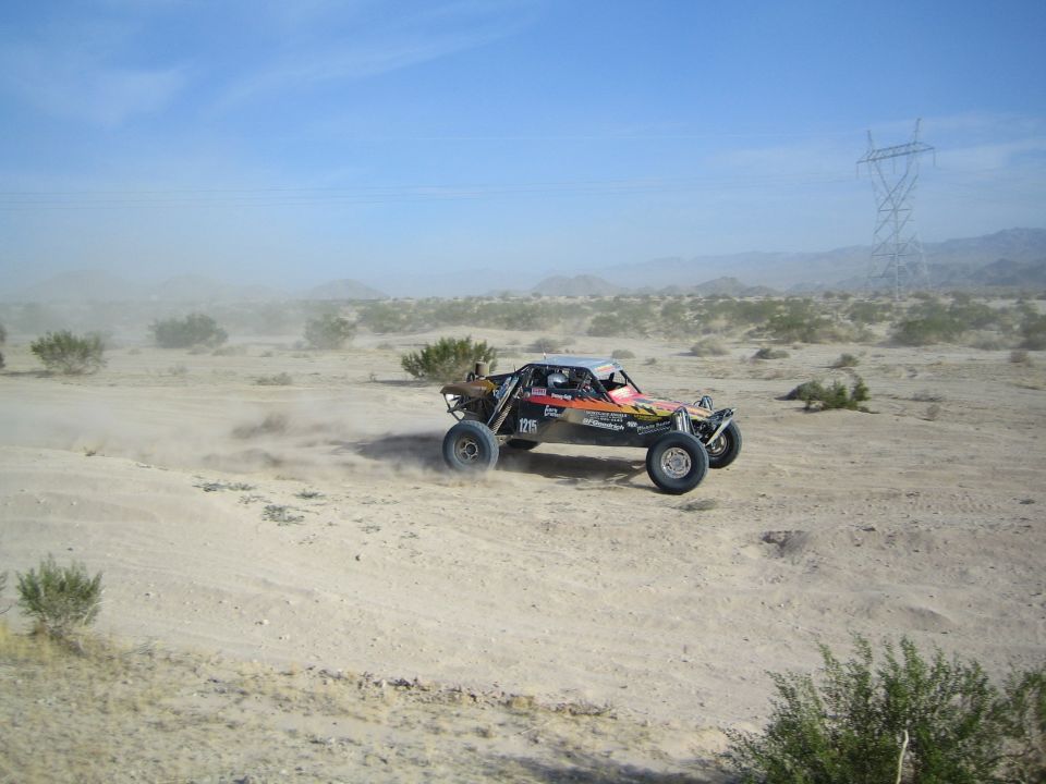 Open-frame desert race buggy speeding past with power line tower behind