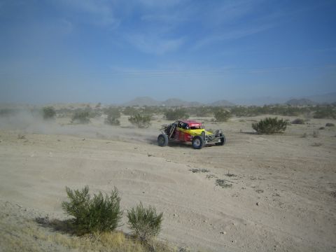 Yellow and red off-road buggy racing through desert dust