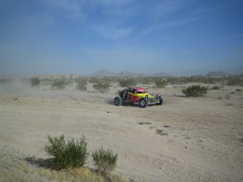 Yellow and red off-road buggy racing through desert dust