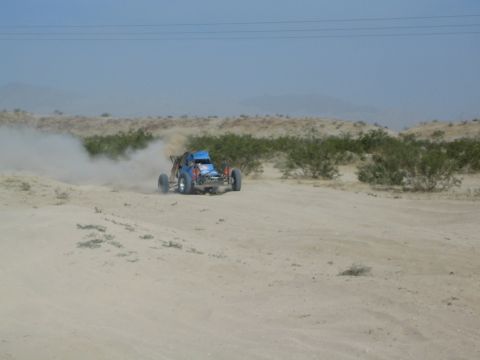 Blue desert race buggy driving across open sandy terrain