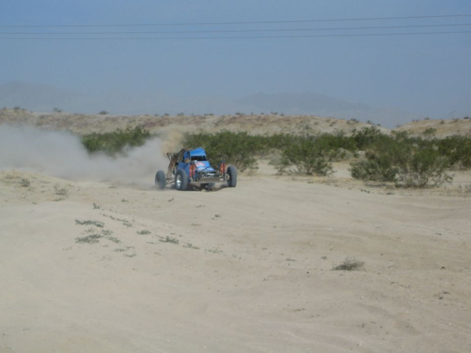 Blue desert race buggy driving across open sandy terrain