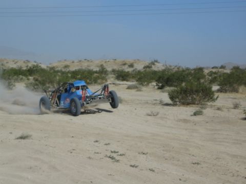 Blue tube-frame desert buggy cornering hard on sand