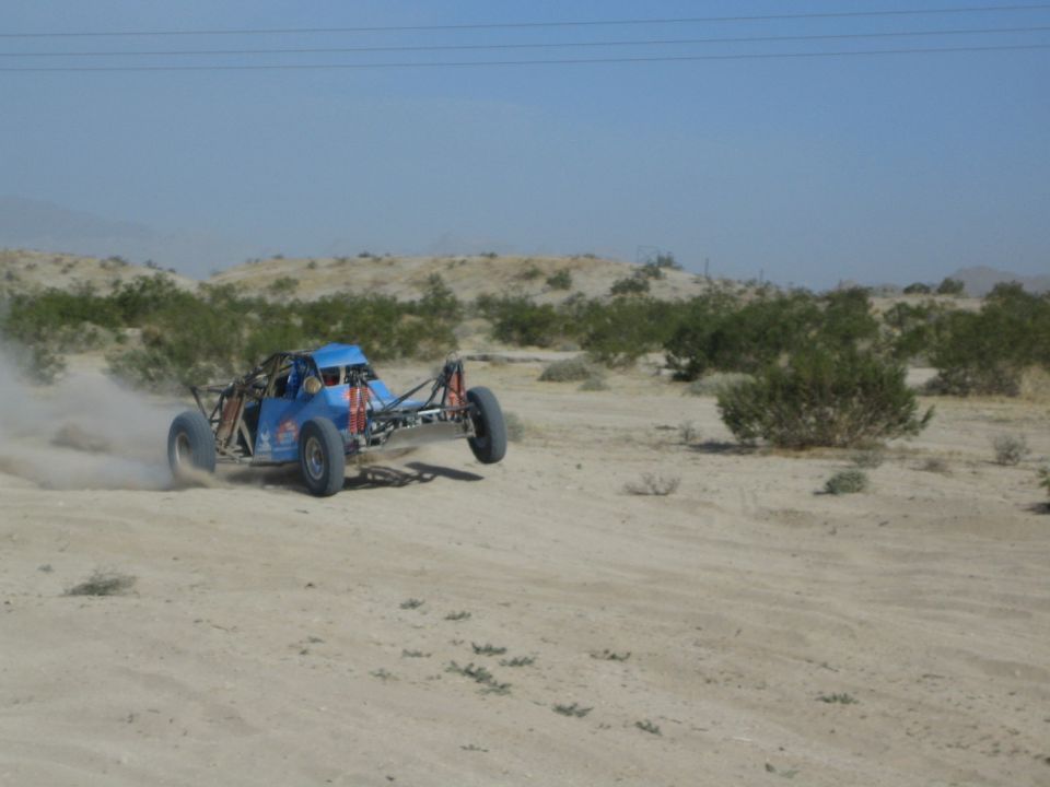 Blue tube-frame desert buggy cornering hard on sand