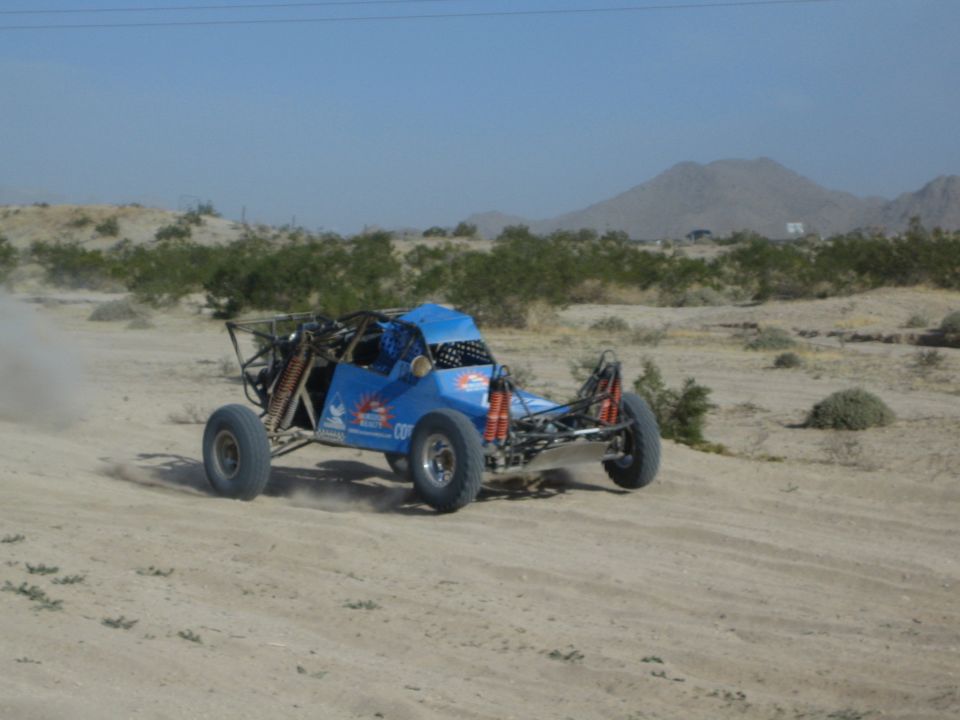 Blue race buggy with shocks visible drifting through desert sand