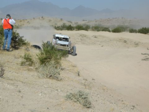 Spectator watches a desert buggy crest a rise on a dusty course