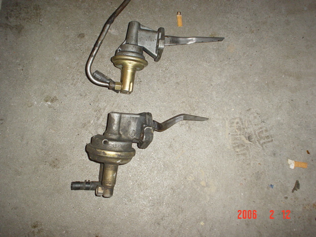 Two mechanical fuel pumps on concrete floor. One has a metal fuel line attached