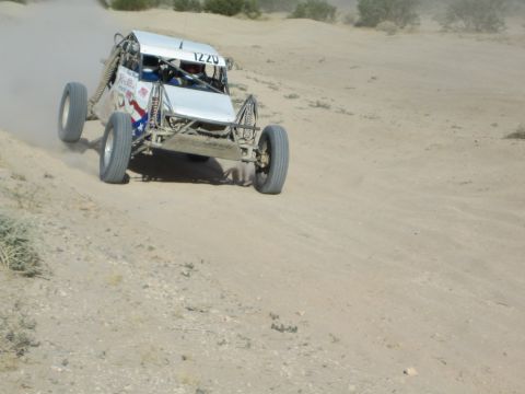 Silver and white race buggy number 1220 charging up a sandy slope