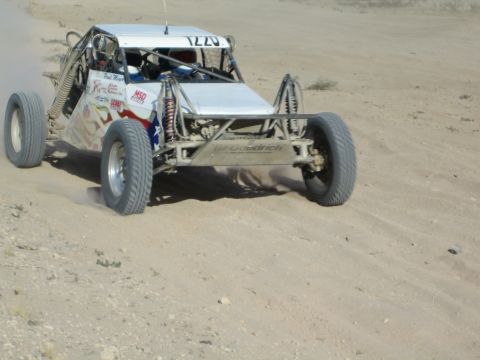 Sponsored white race buggy with Texas flag charging across sand