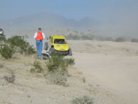 Spectator watches a yellow off-road truck on a dusty desert ridge