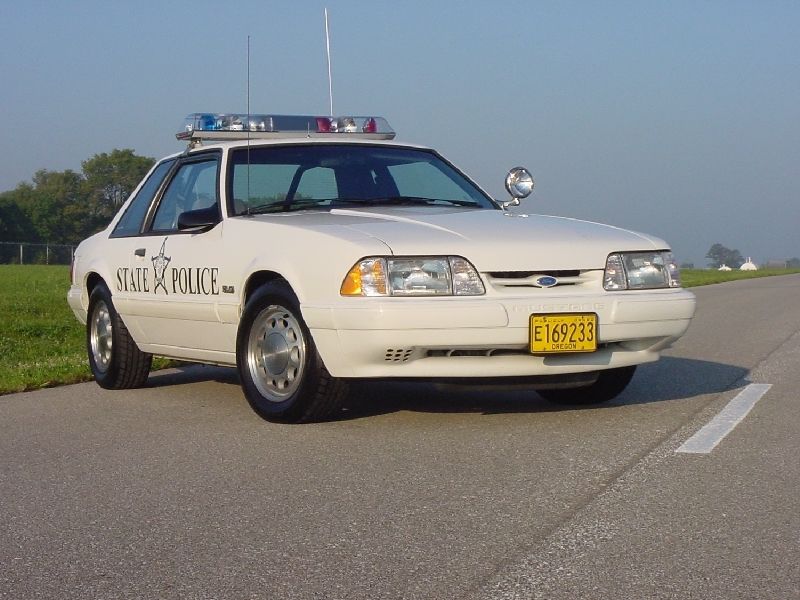 White 1993 Ford Mustang police car with "STATE POLICE" text on the door, parked on asphalt