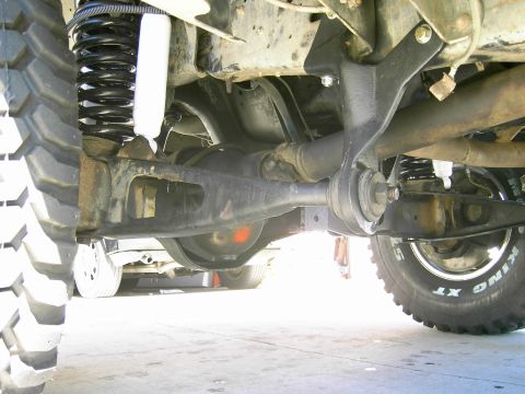 1988 Ford Bronco - Close-up of the suspension and drivetrain components on a lifted truck, with another vehicle in the background.