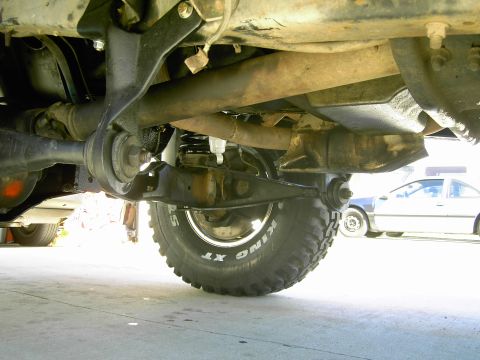 1988 Ford Bronco - The photo shows the undercarriage of a vehicle, focusing on its suspension and a large tire. Another car is parked in the background.