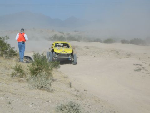 Yellow off-road truck jumping a rise as a spectator looks on
