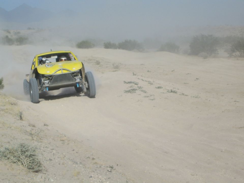 Yellow off-road buggy charging up a dusty sandy slope