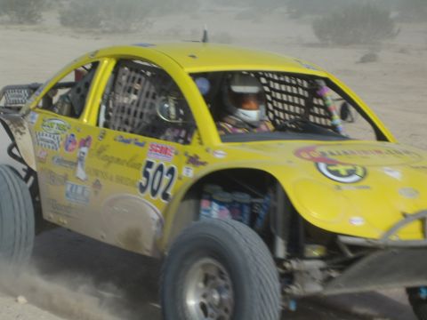 Yellow number 502 off-road race car with caged cockpit and helmeted driver
