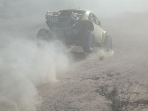 Rear view of yellow race car number 502 climbing through thick dust