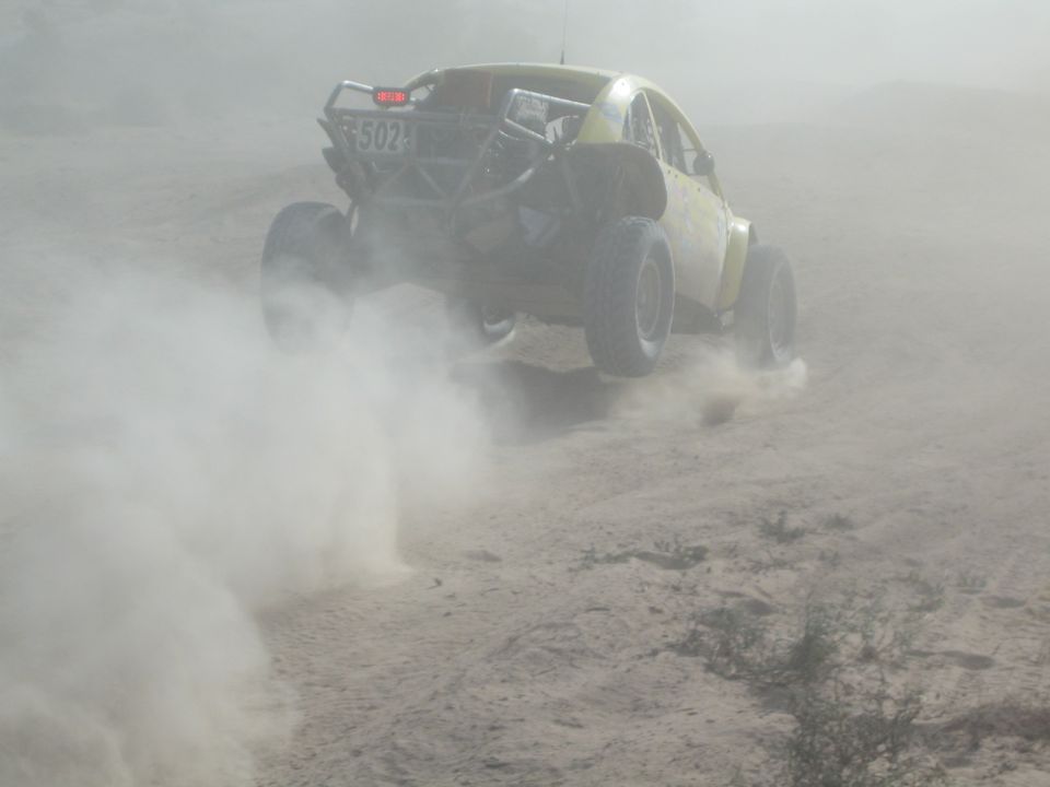 Rear view of yellow race car number 502 climbing through thick dust