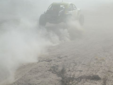 Off-road race car jumping airborne in heavy desert dust