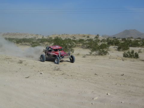 Dark red open-frame buggy racing across open desert