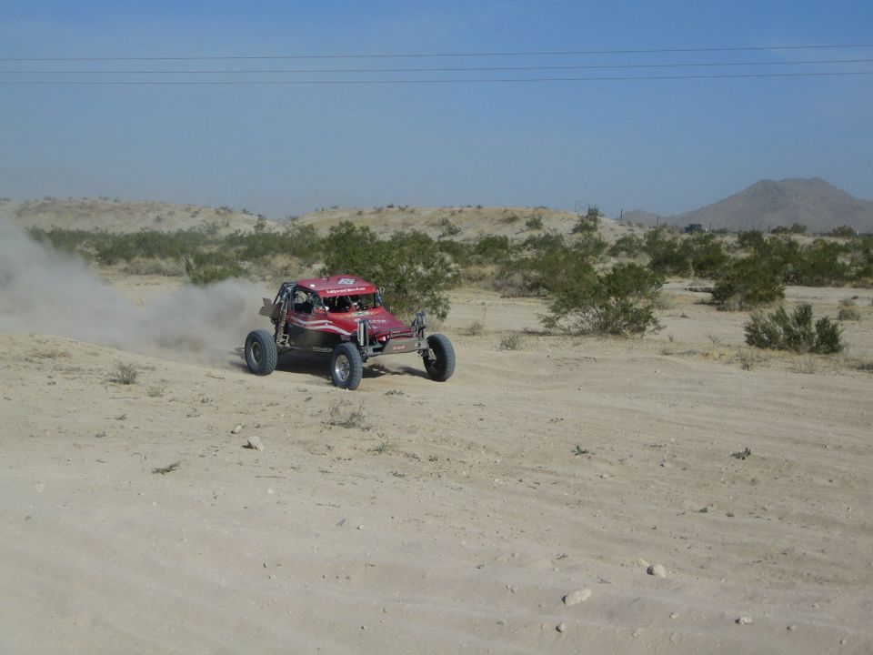 Dark red open-frame buggy racing across open desert