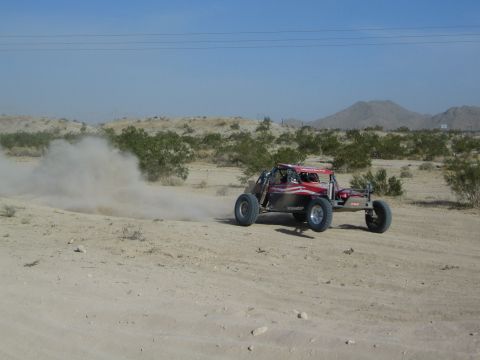 Red single-seat off-road race buggy kicking up dust on a desert trail