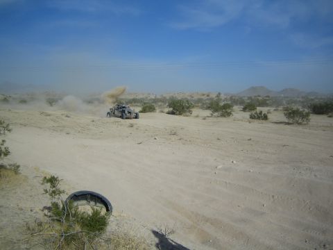 Distant off-road buggy raising a dust cloud across scrubland with a tire in foreground