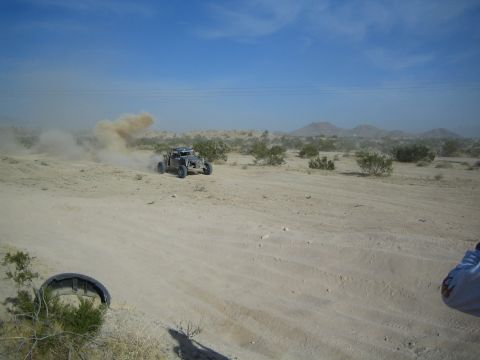 Off-road buggy trailing dust in desert with a spectator at right edge