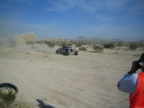 Spectator in orange vest watches off-road buggy raise dust in desert