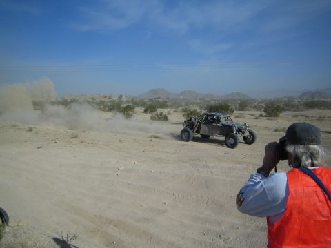 Orange-vested photographer photographs distant off-road buggy in desert