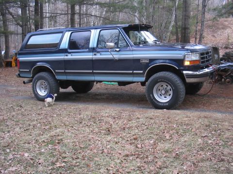 1979 Ford Bronco - A blue Ford Bronco Centurion is parked on a dirt road surrounded by trees.