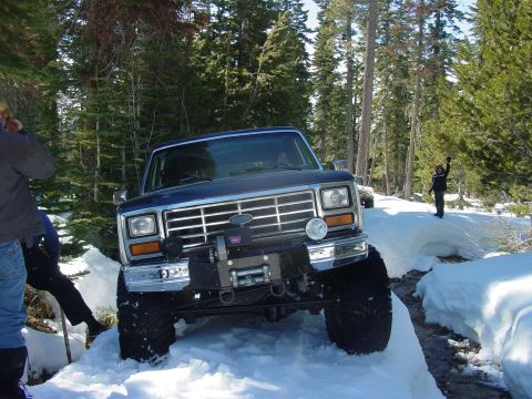 1986 Ford Bronco - A blue Ford Bronco navigates a snowy trail with a winch mounted on the front bumper.