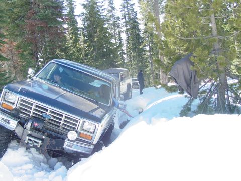 1986 Ford Bronco - A dark blue 1980s Ford Bronco navigates a snowy trail with another vehicle behind it.