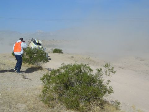 Photographer in orange vest captures a white buggy raising dust in desert