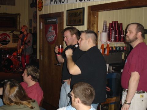 1985 Ford Crown Victoria LTD - A band plays live music in a dimly lit bar while patrons watch and socialize.