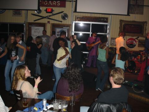 1985 Ford Crown Victoria LTD - A lively scene unfolds as people dance and a band plays music in a bar or club setting.