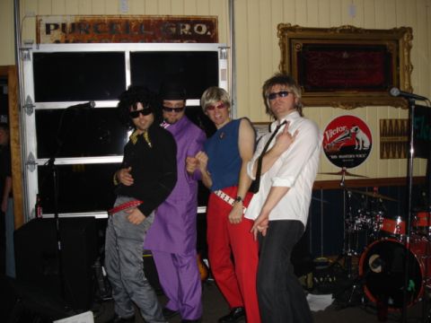 1985 Ford Crown Victoria LTD - A group of men dressed in 1980s-inspired costumes pose for a photo indoors.
