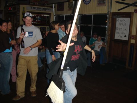 1985 Ford Crown Victoria LTD - A group of people are socializing in a bar, with one person playfully posing with a broom.