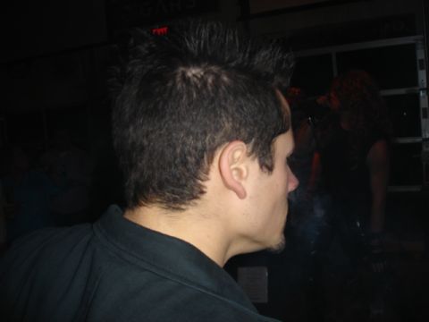 1985 Ford Crown Victoria LTD - A man with a mohawk hairstyle is seen from the side, smoking in a dimly lit indoor setting.