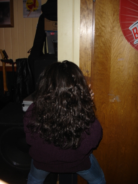 1985 Ford Crown Victoria LTD - A woman's back is visible as she reaches for a wooden door in a room that appears to be a bar or lounge.