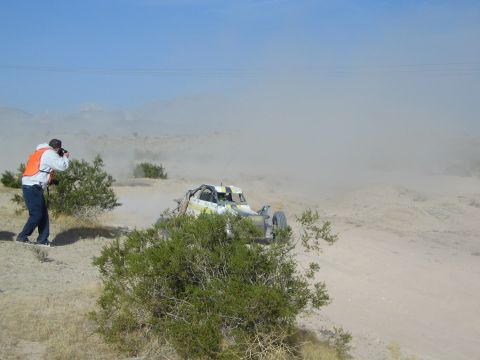 White and yellow off-road buggy in dust with photographer at left