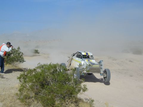 White and yellow off-road buggy with raised front wheels in desert dust