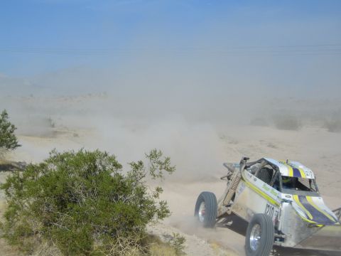 White and yellow off-road race buggy speeding through heavy desert dust