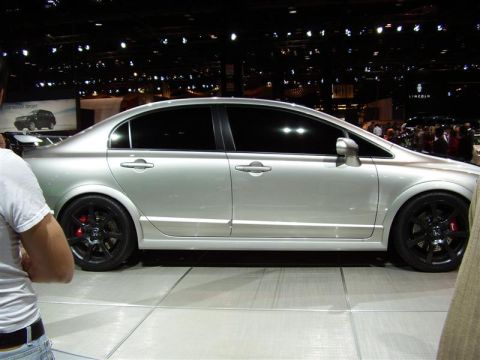 1997 Ford Taurus - A silver sedan is displayed indoors on a white platform with a crowd in the background.