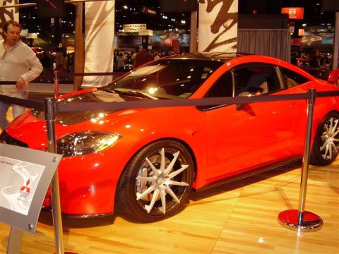 1997 Ford Taurus - Red sports coupe on display at an auto show, with a Mitsubishi logo visible on a nearby sign.