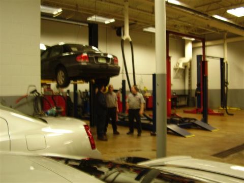 1997 Ford Taurus - Mechanics observe a car elevated on a lift inside a service bay.